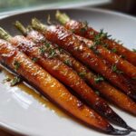 Close-up of perfectly glazed roasted baby carrots drizzled with sauce and topped with fresh thyme.