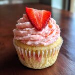 A single, delicious strawberry cupcake topped with pink frosting and a fresh strawberry slice.