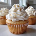 Close-up of a perfectly baked vanilla cupcake topped with a generous swirl of white vanilla frosting.