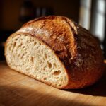 A freshly baked loaf of whole wheat bread, sliced in half to show the airy crumb structure, resting on a wooden board.
