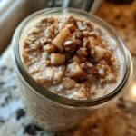 Overhead close-up of creamy apple cinnamon overnight oats topped with diced apples and cinnamon in a glass jar.