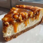A decadent slice of apple pie cheesecake topped with chunky caramel sauce drizzled down the sides.