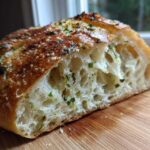 Close-up of a slice of artisan bread showing the open, airy crumb and herb topping.