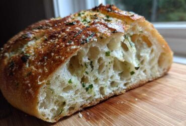 Close-up of a slice of artisan bread showing the open, airy crumb and herb topping.