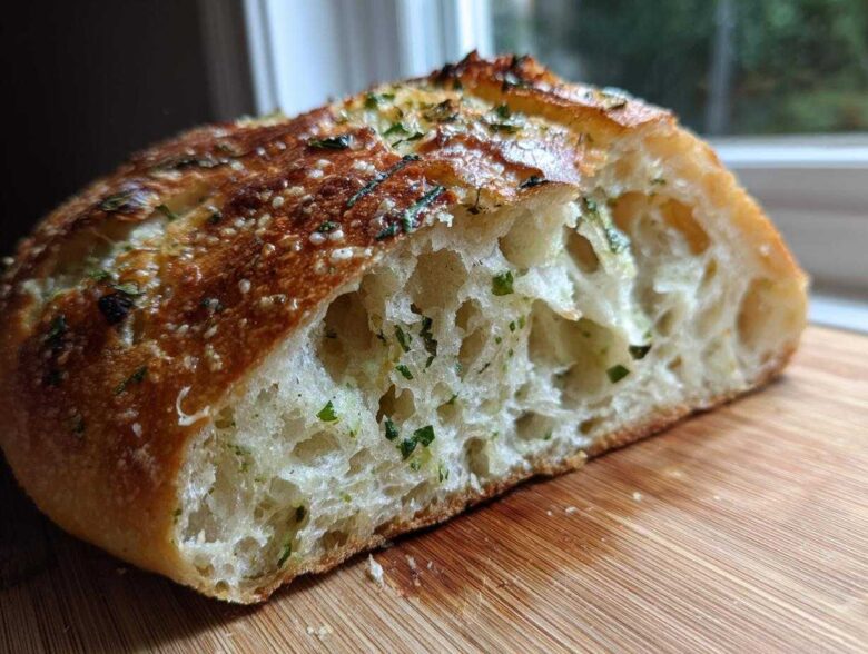 Close-up of a slice of artisan bread showing the open, airy crumb and herb topping.