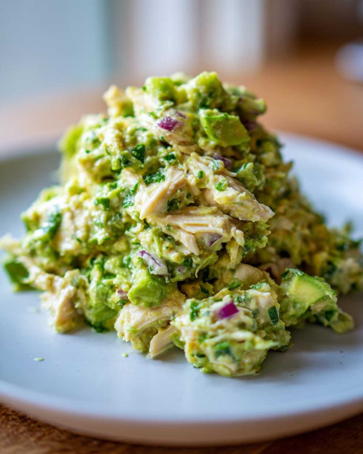 Close-up of a mound of creamy avocado chicken salad featuring chunks of chicken, diced avocado, and red onion.