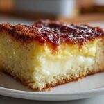 A close-up view of a moist slice of bee sting cake featuring a thick layer of cream filling and a caramelized honey topping.