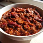 Close-up of a rich, thick bowl of chili, featuring ground meat and kidney beans, ready to eat.
