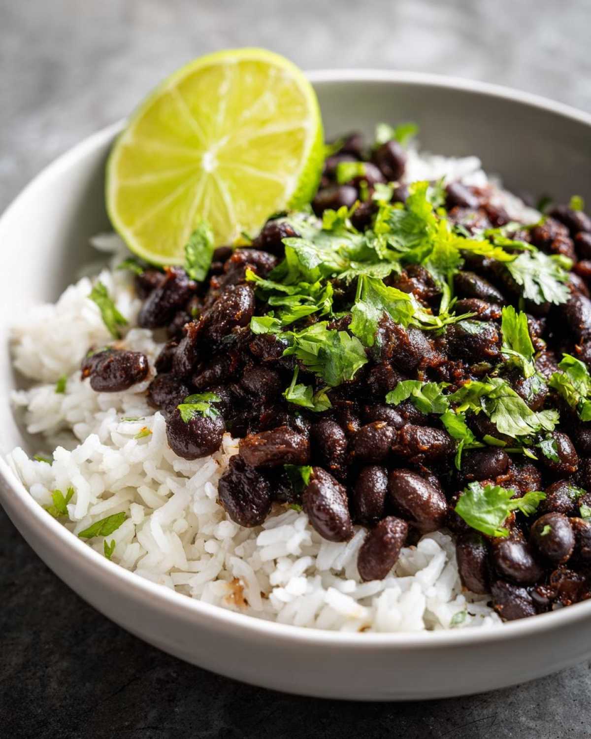 Close-up of a bowl of flavorful black beans and rice topped with fresh cilantro and a lime wedge.