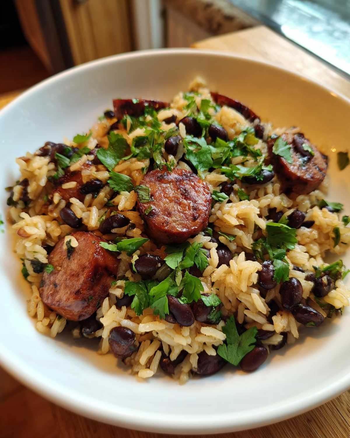 A white bowl filled with flavorful black beans and rice, topped with sliced smoked sausage and fresh parsley.