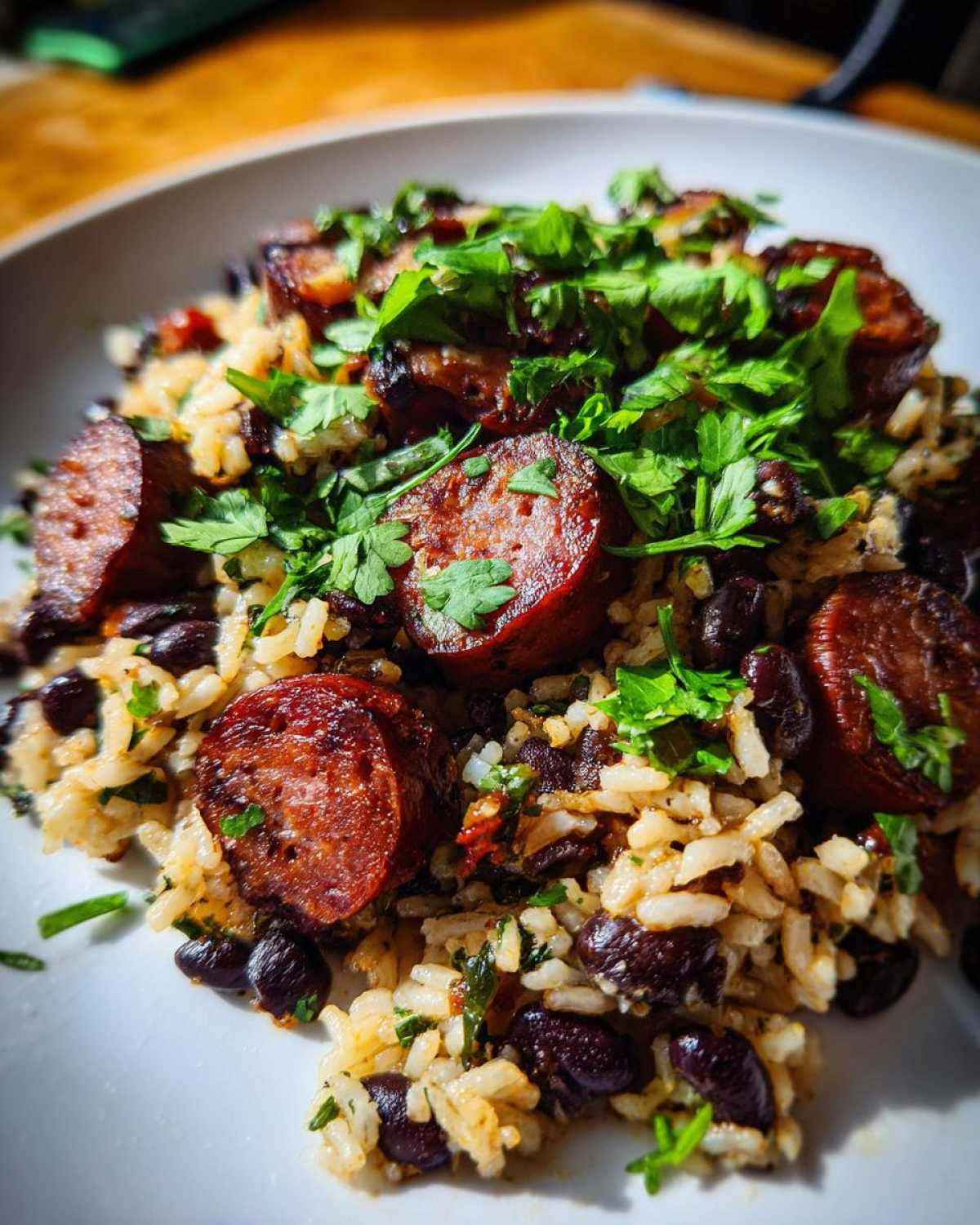 Close-up of flavorful black beans and rice topped with sliced, seared sausage and fresh cilantro.