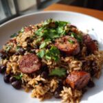 A close-up of flavorful black beans and rice mixed with slices of browned sausage and topped with fresh cilantro.