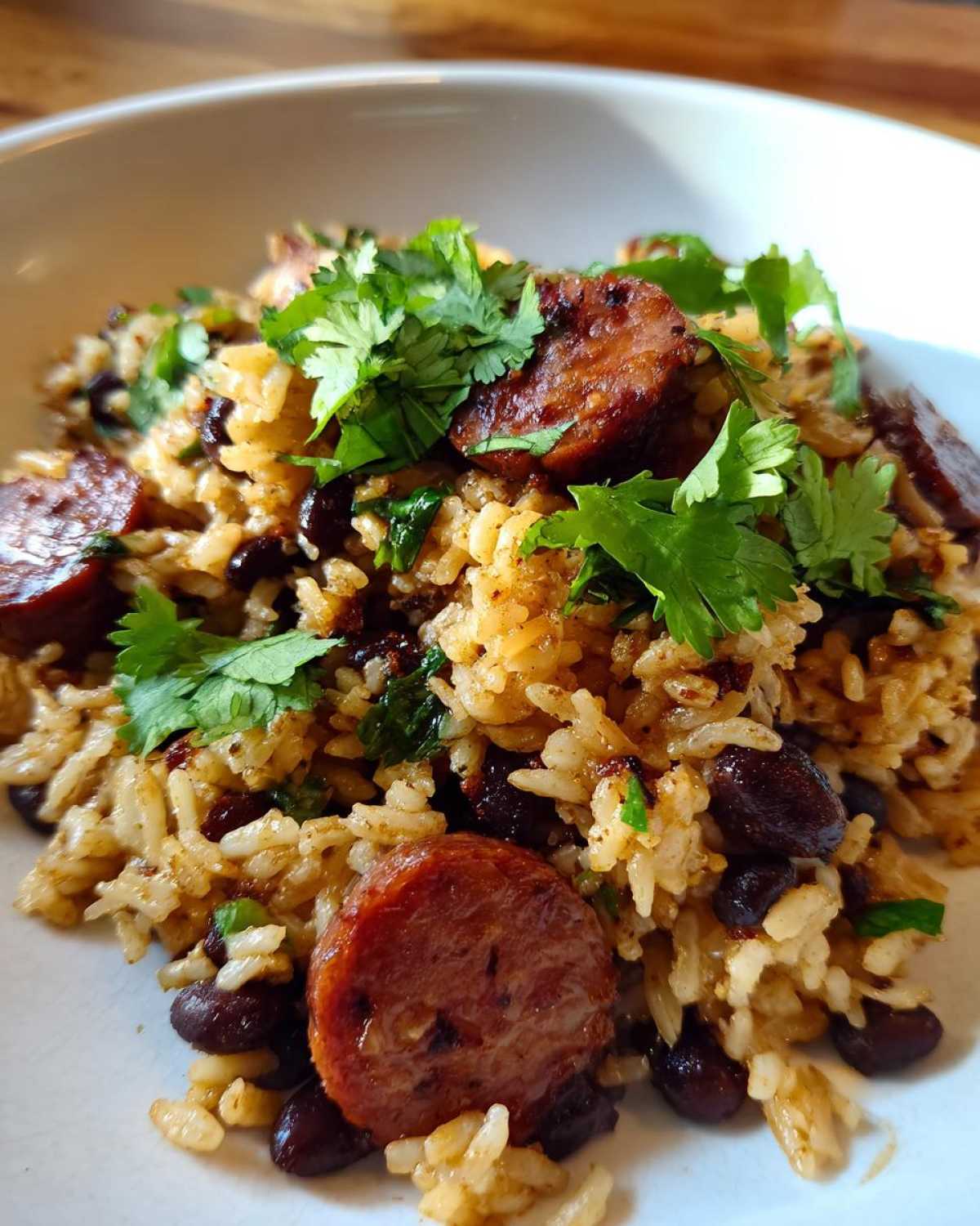 Close-up of flavorful black beans and rice mixed with sliced, browned sausage and topped with fresh cilantro.