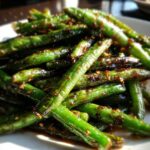 A close-up shot of bright green, blistered chinese green beans with garlic sauce coating them.