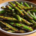 Close-up of blistered chinese green beans with garlic sauce piled high in a light gray serving bowl.