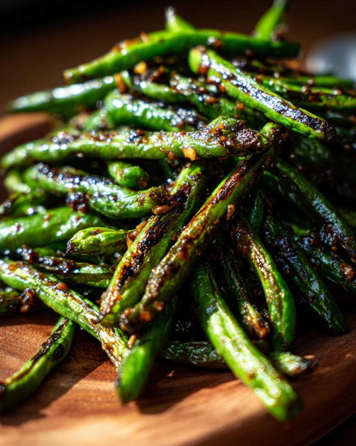 A pile of blistered chinese green beans with garlic sauce, showing charred edges and glossy coating.