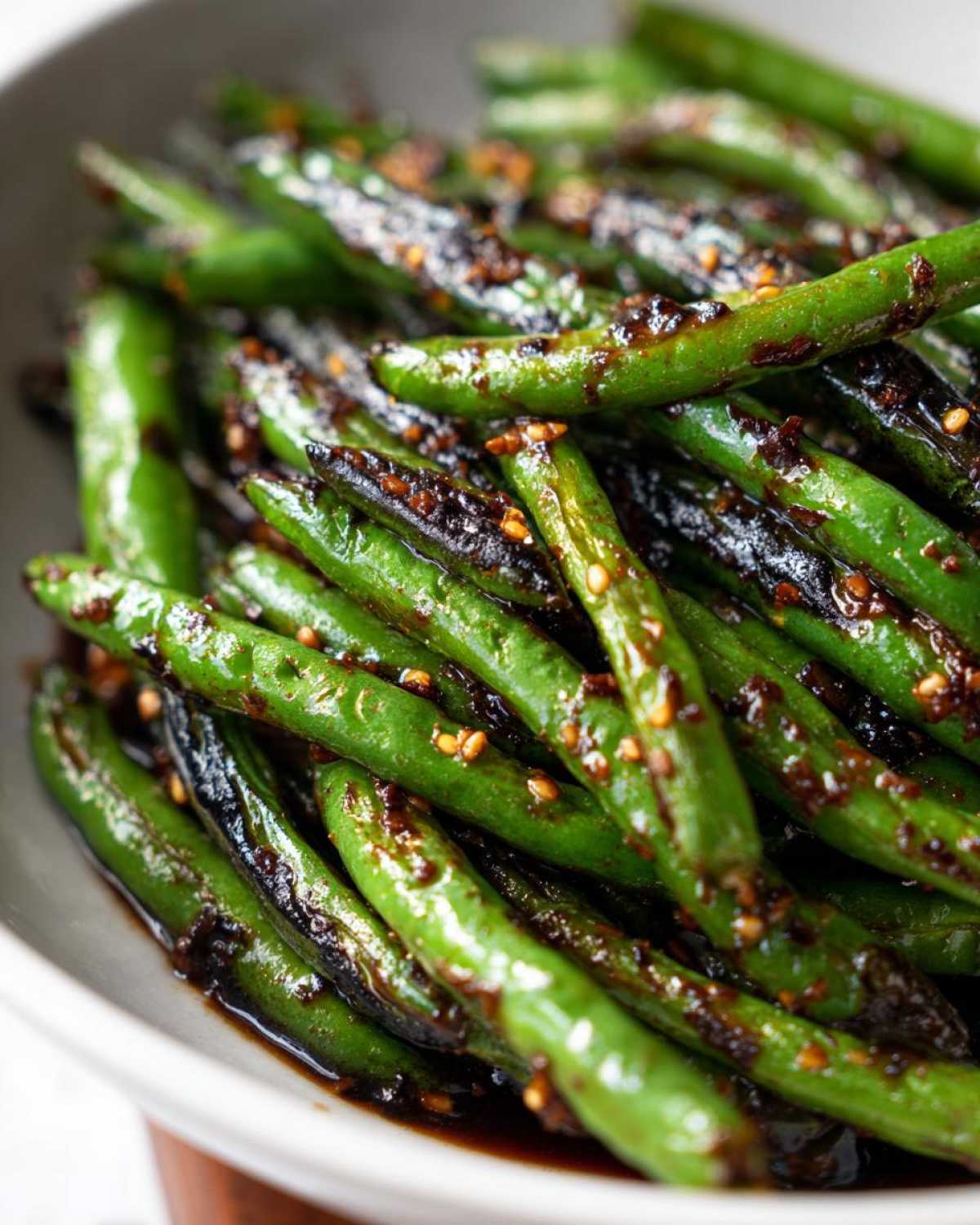 Close-up of vibrant green beans coated in a dark, savory garlic sauce and sesame seeds.