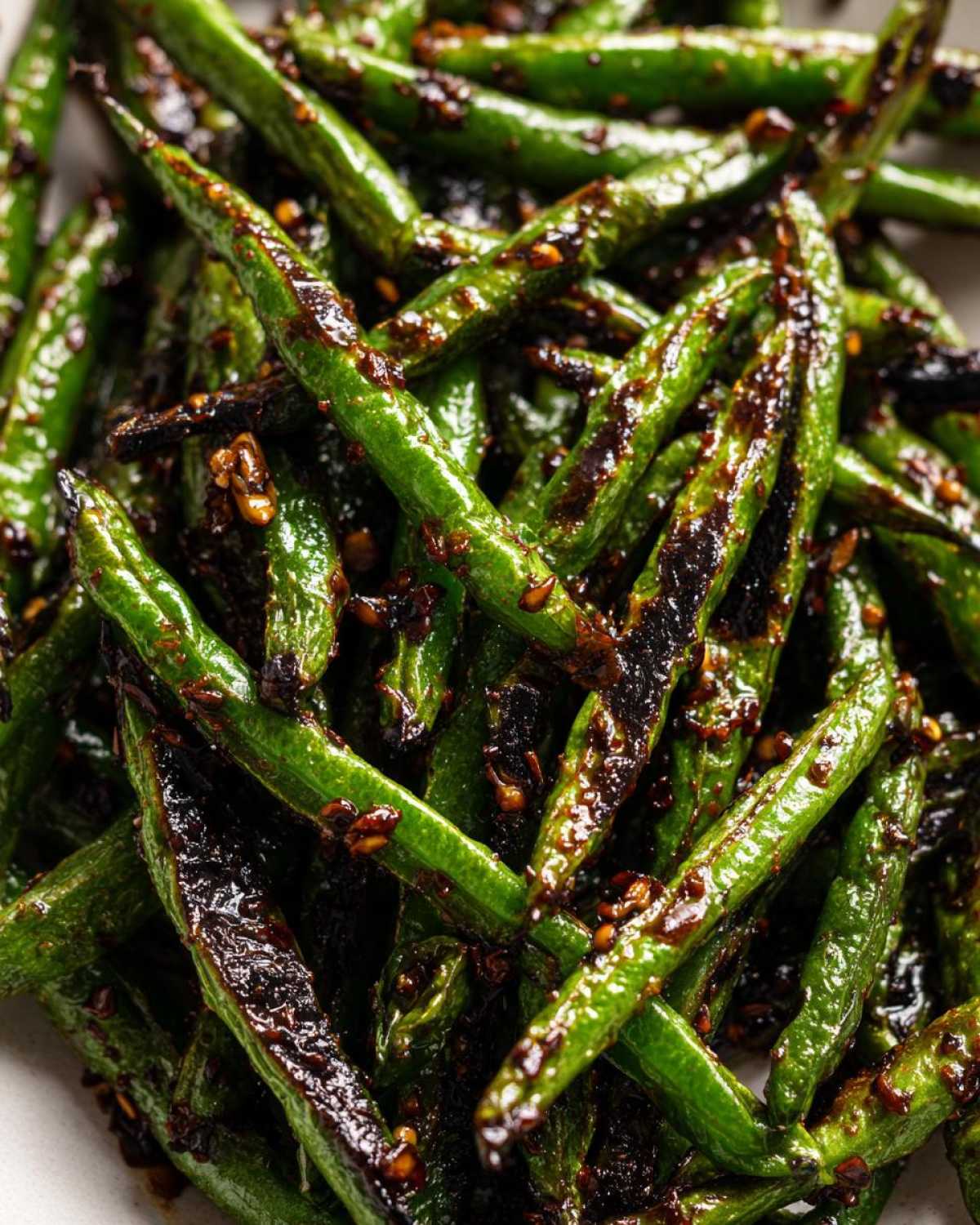 Close-up of bright green, blistered chinese green beans with garlic sauce and chili flakes.