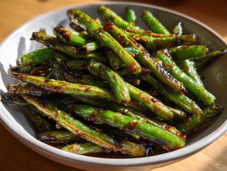 Close-up of blistered chinese green beans with garlic sauce piled high in a light gray serving bowl.