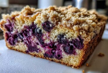 Close-up of a slice of blueberry banana bread showing a moist crumb, bursting blueberries, and a crunchy streusel topping.