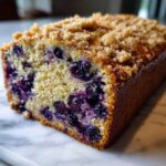 A moist slice of blueberry banana bread featuring vibrant blueberries and a crunchy brown sugar streusel topping.