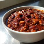 Close-up of a hearty bowl of chili, rich with ground meat and dark red kidney beans, showcasing the best chili recipe texture.