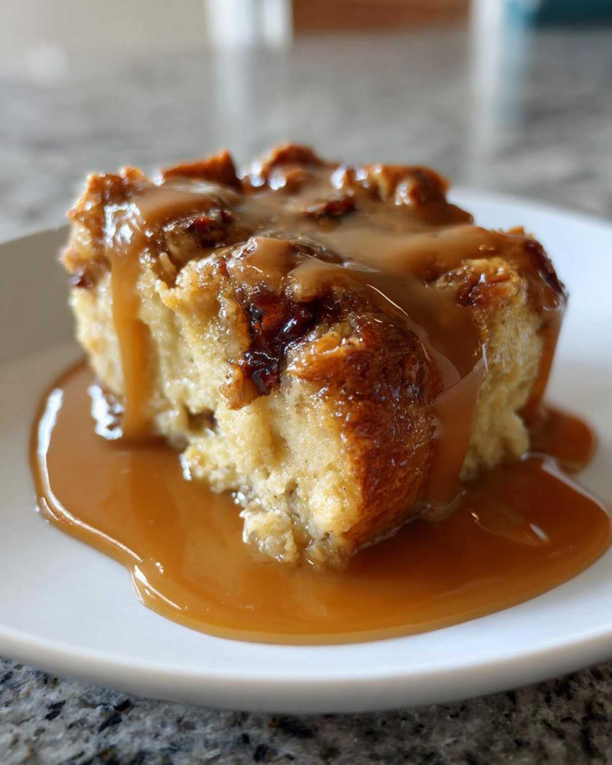 A close-up of a square serving of bread pudding with bourbon sauce generously drizzled over the top.