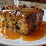 A rich slice of bread pudding with bourbon sauce generously drizzled over the top and pooling on the white plate.