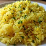 Close-up of fluffy, bright yellow mediterranean rice seasoned and topped with chopped fresh parsley.
