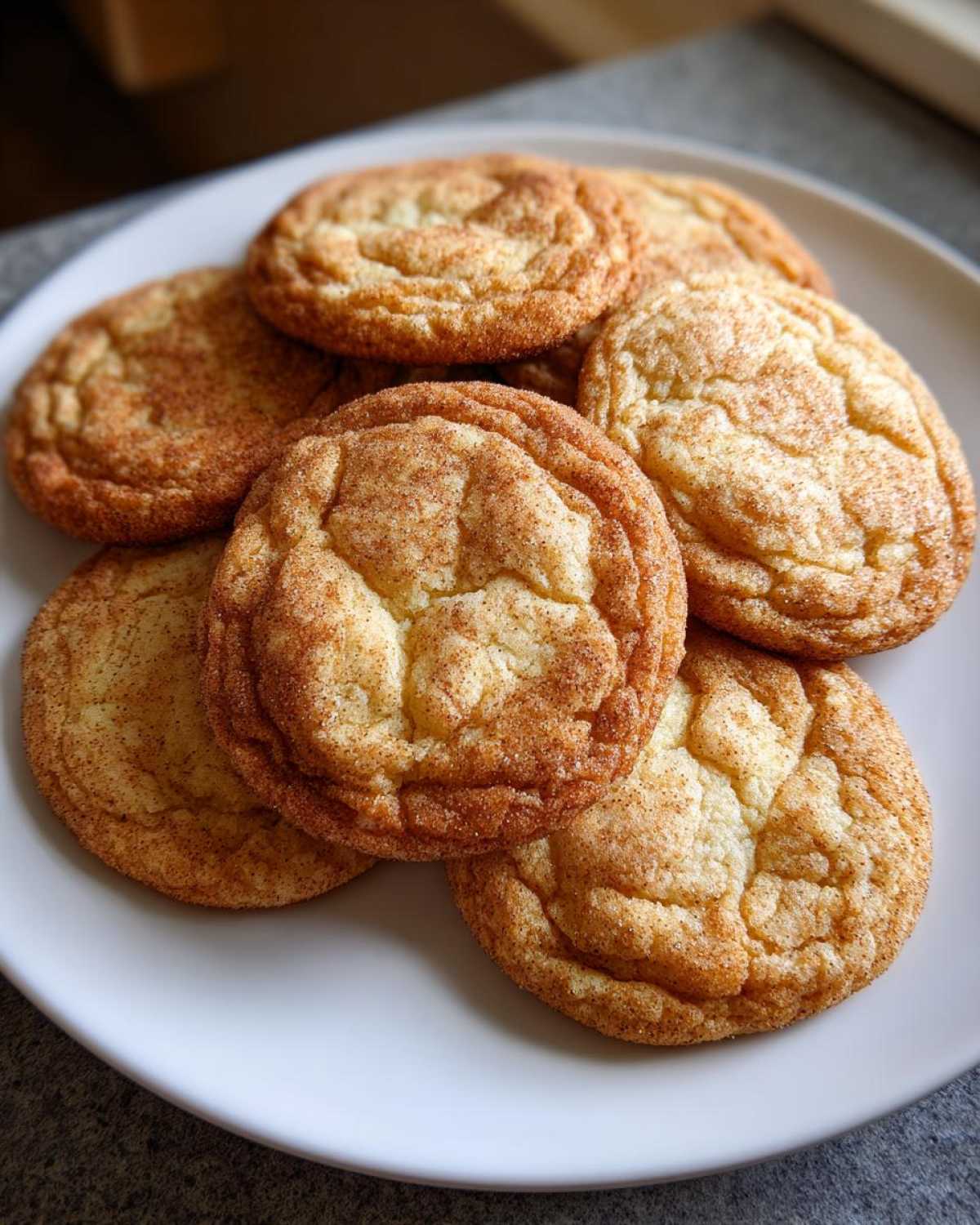 A close-up of several soft, crinkled brown butter sugar cookies dusted heavily with cinnamon sugar on a white plate.
