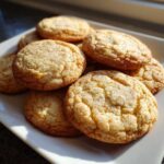 A close-up stack of freshly baked brown butter sugar cookies with cracked tops, resting on a white serving plate.