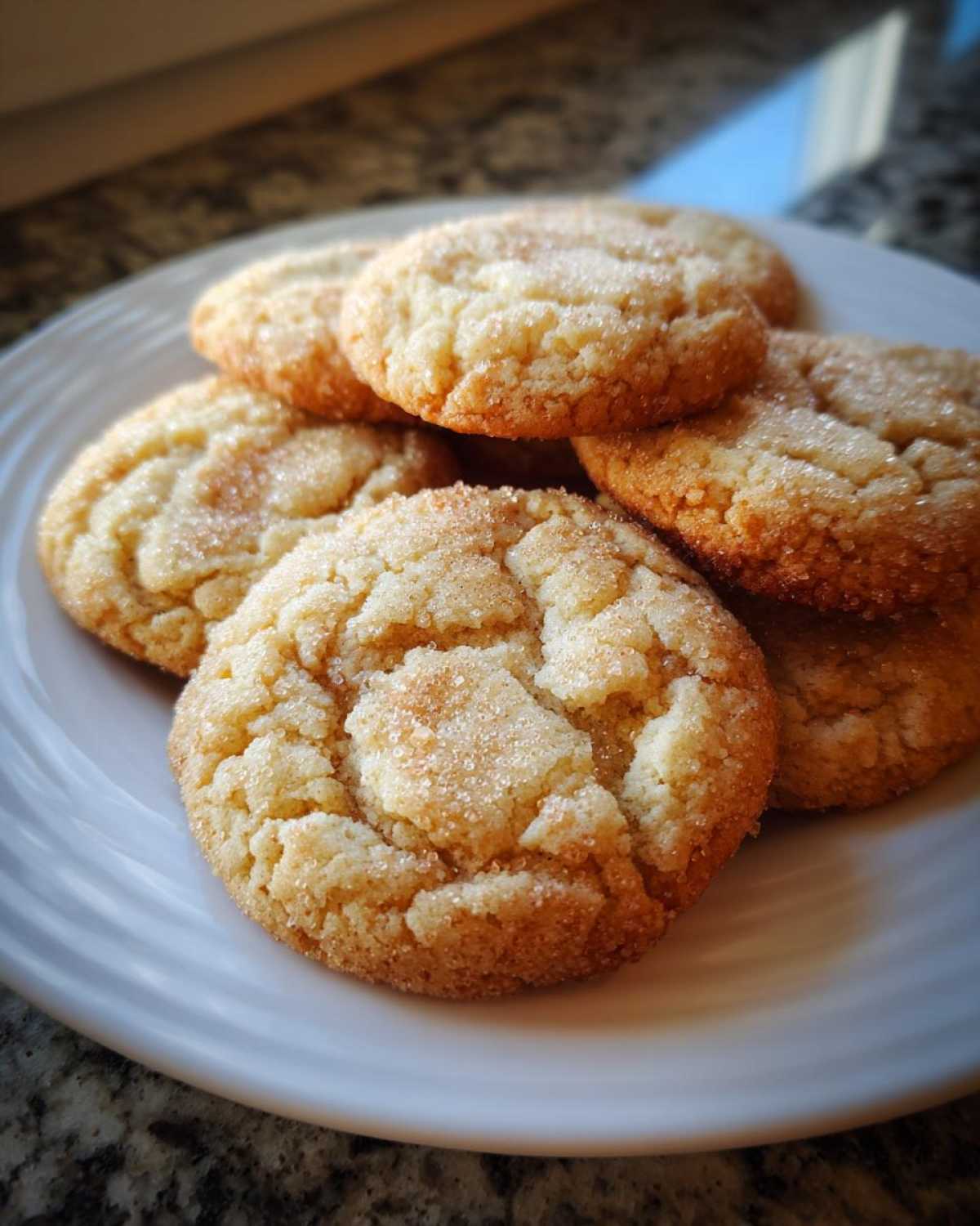A stack of freshly baked brown butter sugar cookies coated in sparkling sugar on a white plate.