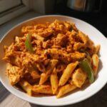 Close-up of creamy Cajun chicken pasta with penne, chicken pieces, and green peppers in a white bowl.