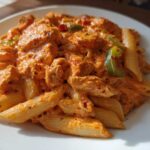 Close-up of creamy Cajun chicken pasta featuring penne noodles, chicken pieces, and green bell peppers.