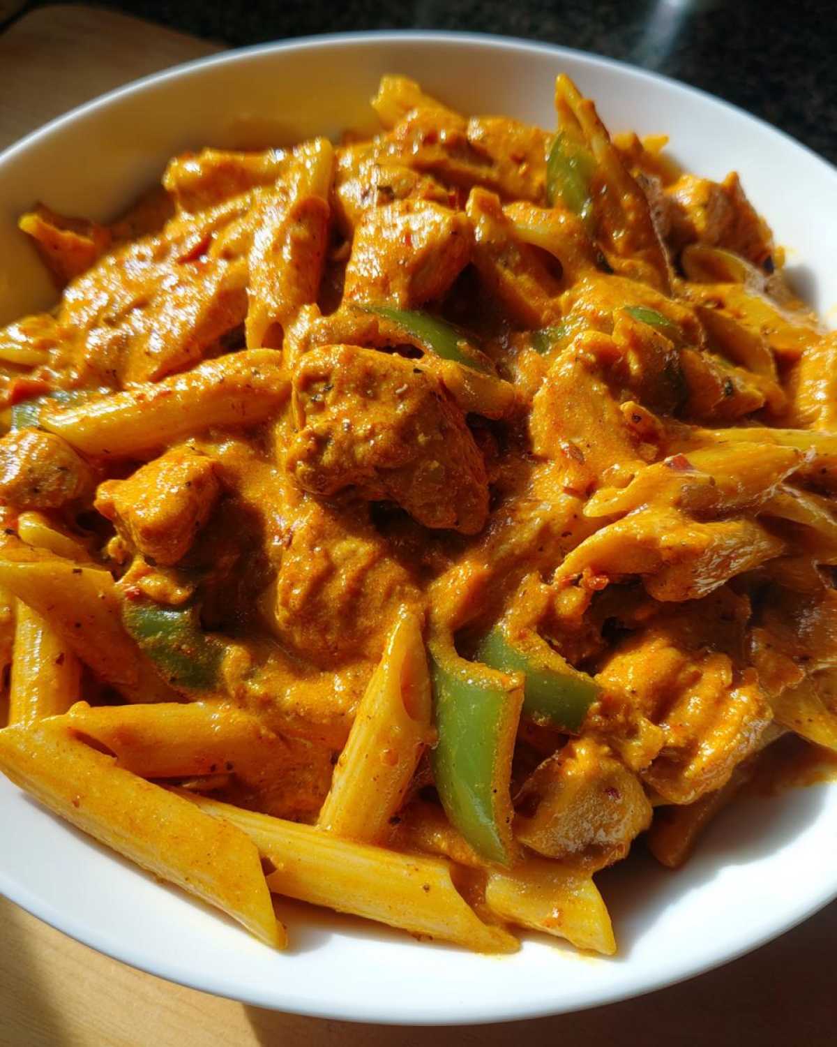 Close-up of creamy Cajun chicken pasta with penne, chicken chunks, and green bell peppers in a white bowl.