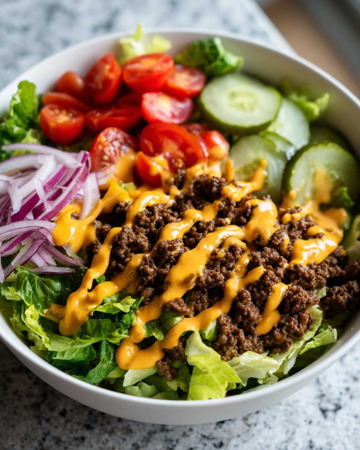 A close-up of a delicious cheeseburger bowl featuring seasoned ground beef, lettuce, tomatoes, onions, and special sauce.