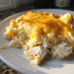 A close-up serving of cheesy chicken and rice casserole topped with melted cheddar cheese.
