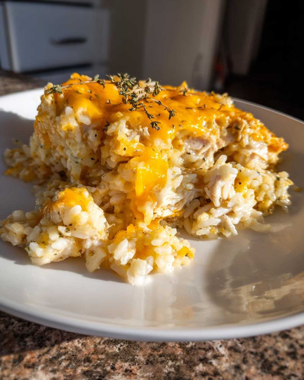 A scoop of cheesy chicken and rice casserole topped with melted cheddar and fresh thyme on a white plate.