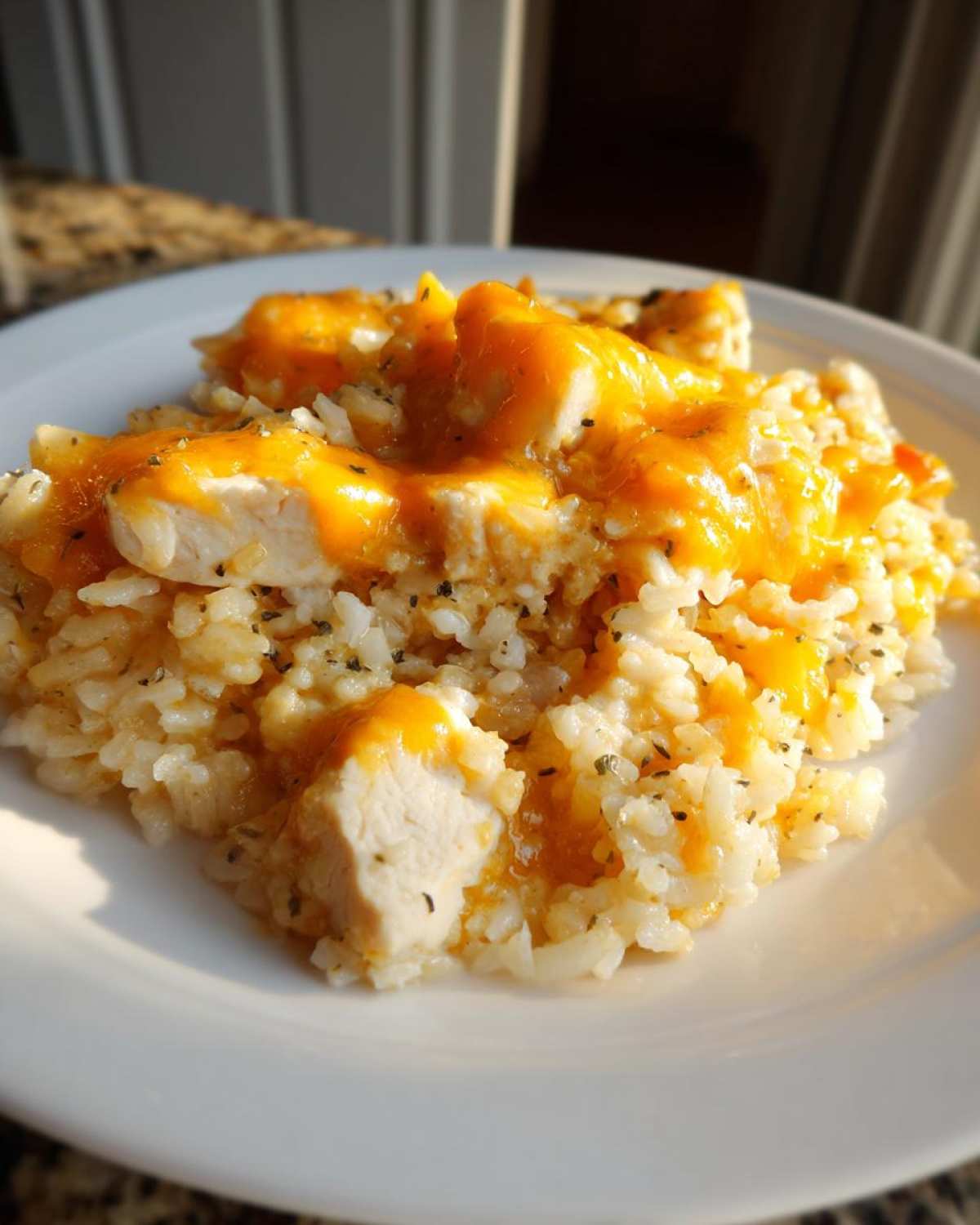 Close-up of a serving of cheesy chicken and rice, featuring chunks of white chicken breast covered in melted orange cheese sauce over seasoned white rice.