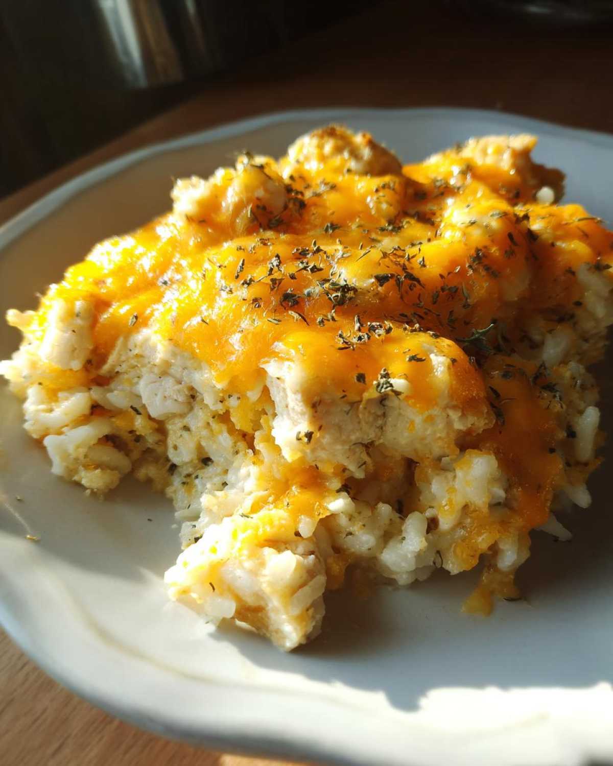 A close-up serving of cheesy chicken and rice topped with melted cheddar and dried herbs.