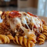 Close-up of a serving of pizza casserole featuring rotini pasta, meat sauce, and melted, stringy mozzarella cheese topped with pepperoni.