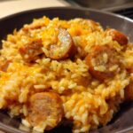 Close-up of cheesy sausage and rice mixture served in a dark brown bowl.