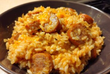 Close-up of cheesy sausage and rice mixture served in a dark brown bowl.