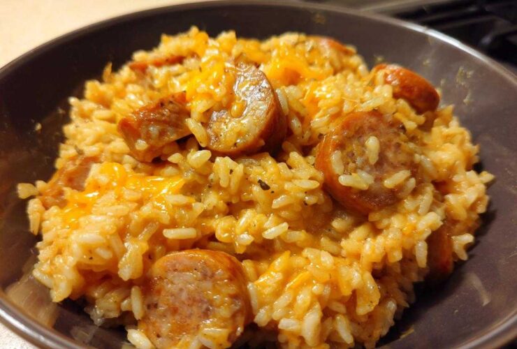 Close-up of cheesy sausage and rice mixture served in a dark brown bowl.