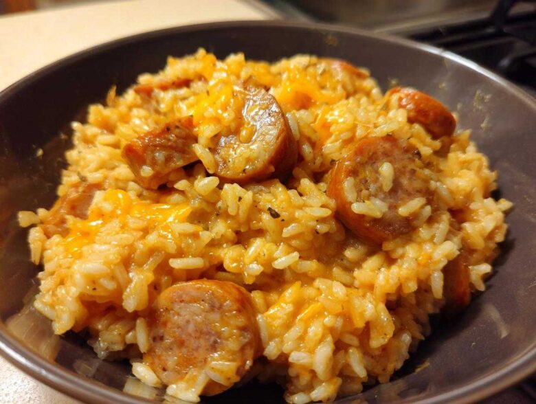 Close-up of cheesy sausage and rice mixture served in a dark brown bowl.