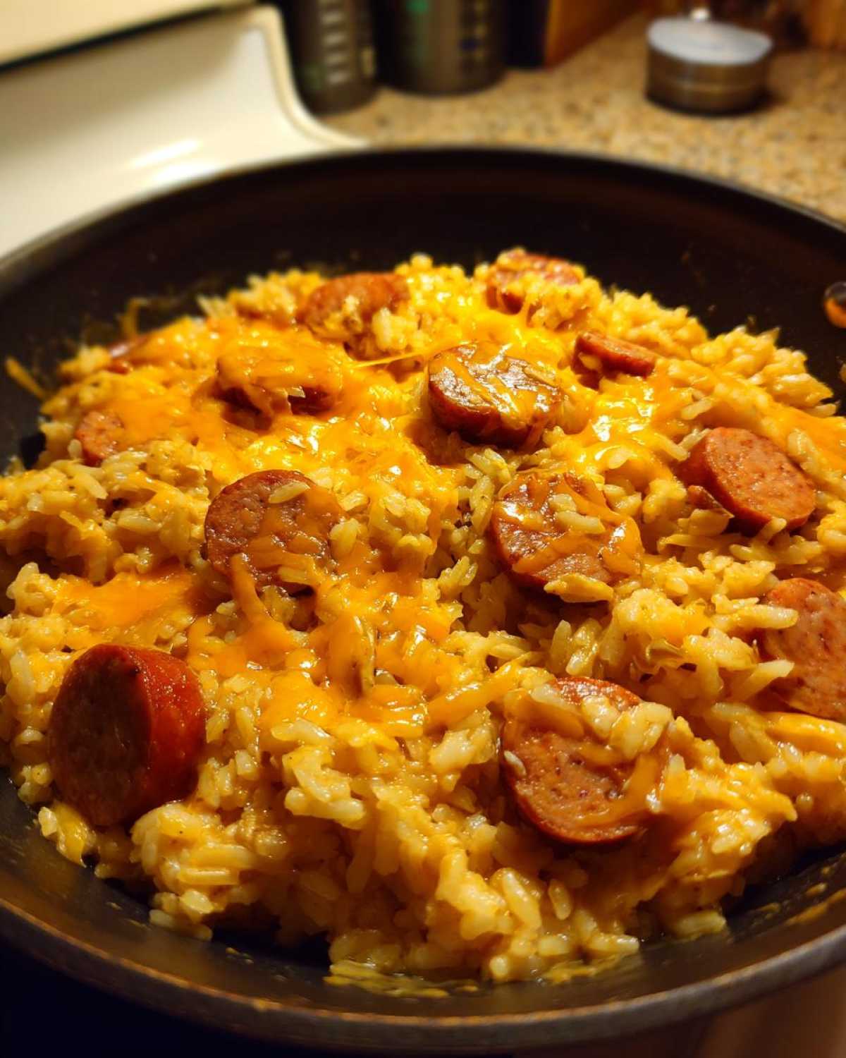 Close-up of cheesy sausage and rice mixture bubbling in a black skillet, topped with melted cheddar.