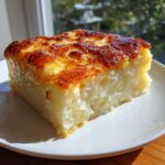 A square slice of chewy cassava cake with a beautifully caramelized, golden-brown topping, served on a white plate.