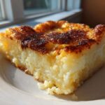 A close-up of a square slice of chewy cassava cake with a beautifully caramelized, dark golden brown top, sitting on a white plate.