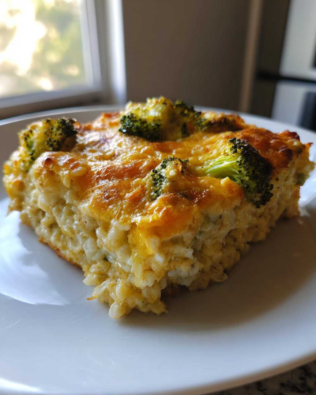 A close-up of a square serving of chicken broccoli rice casserole topped with melted golden cheese and broccoli florets.