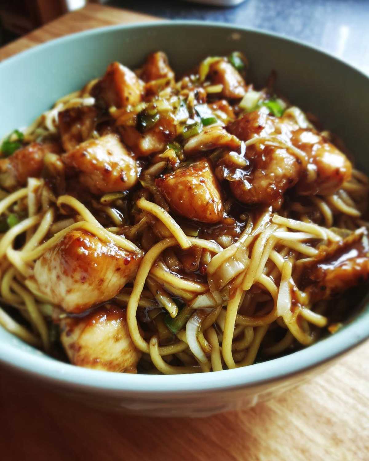 Close-up of a light blue bowl filled with glossy chicken chow mein recipe featuring tender chicken pieces and noodles.